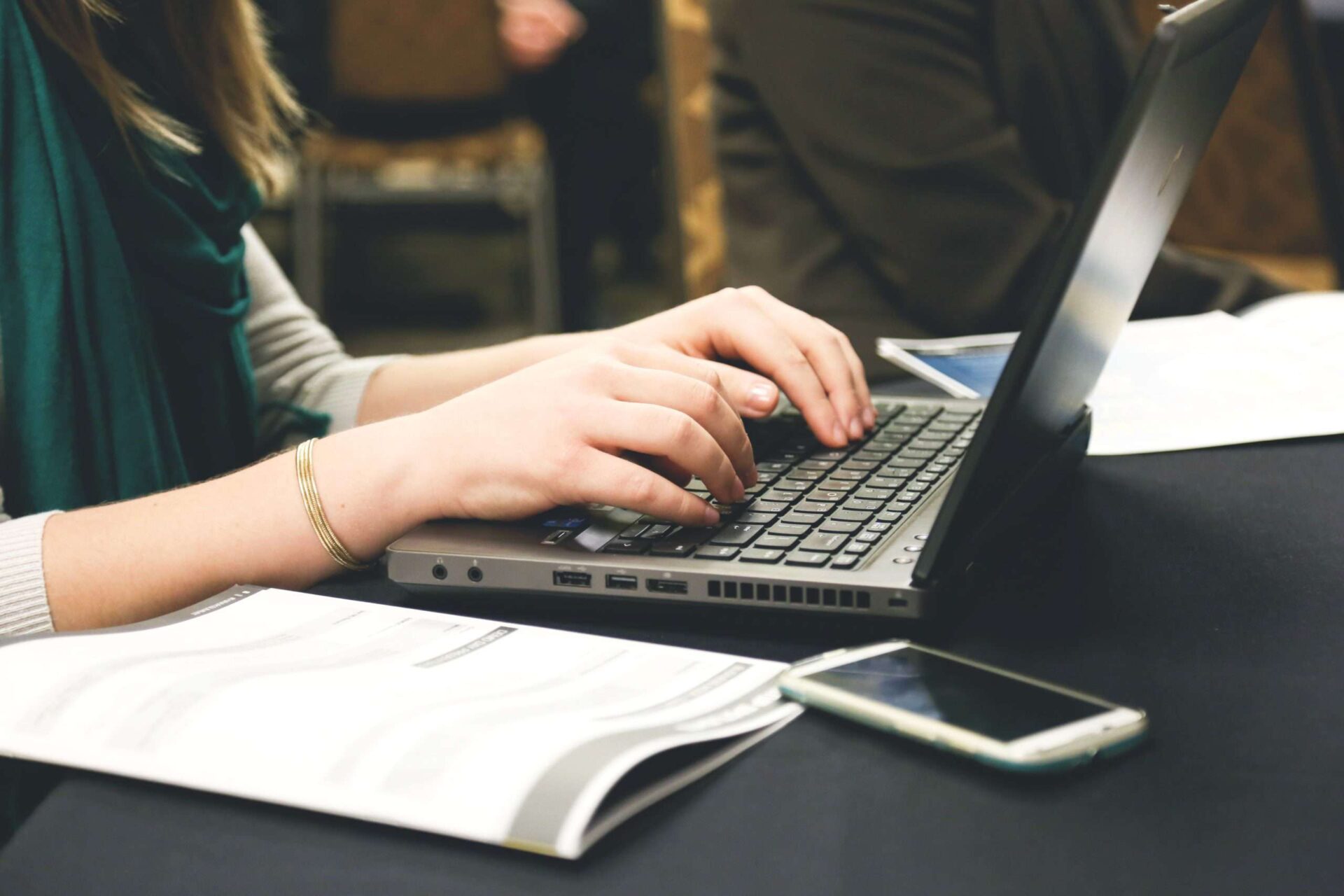 close up of women working at a laptop with paperwork and a phone next to her