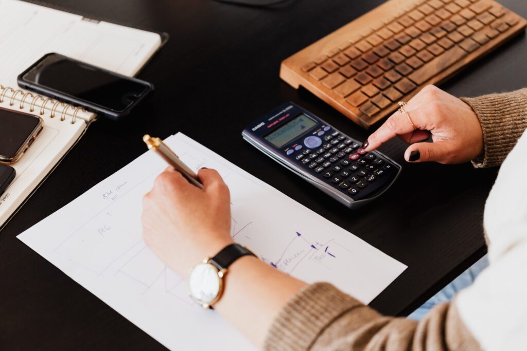 Closeup of hands as someone presses buttons on a calculator and writing on a sheet of paper