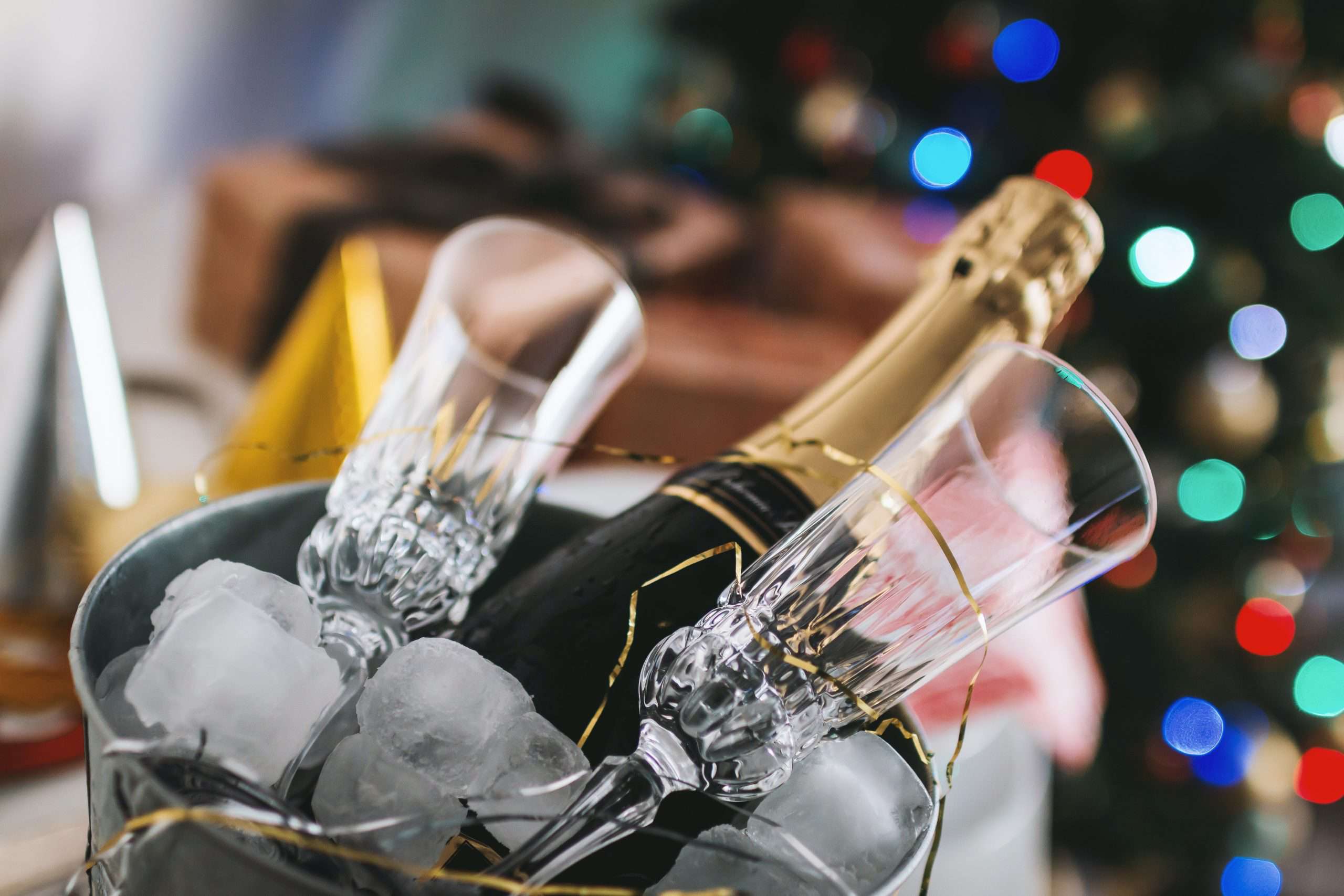 Bottle of champagne in an ice bucket with two glasses and Christmas tree in the background
