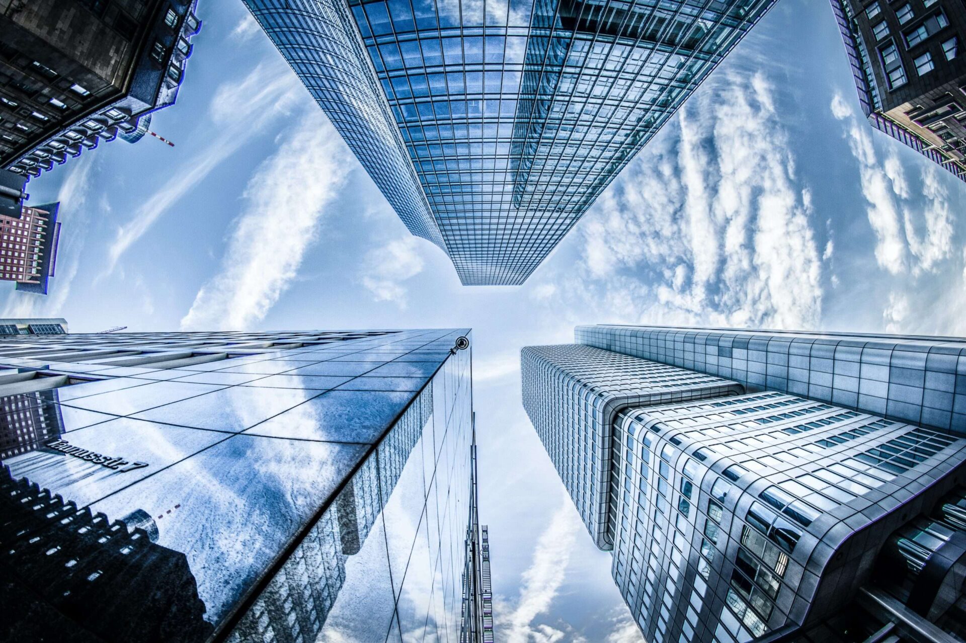 Straight up shot from the middle of three skyscrapers showing a cloudy blue sky