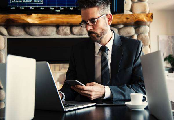 Businessman working at a laptop and using his mobile phone with a coffee cup nearby