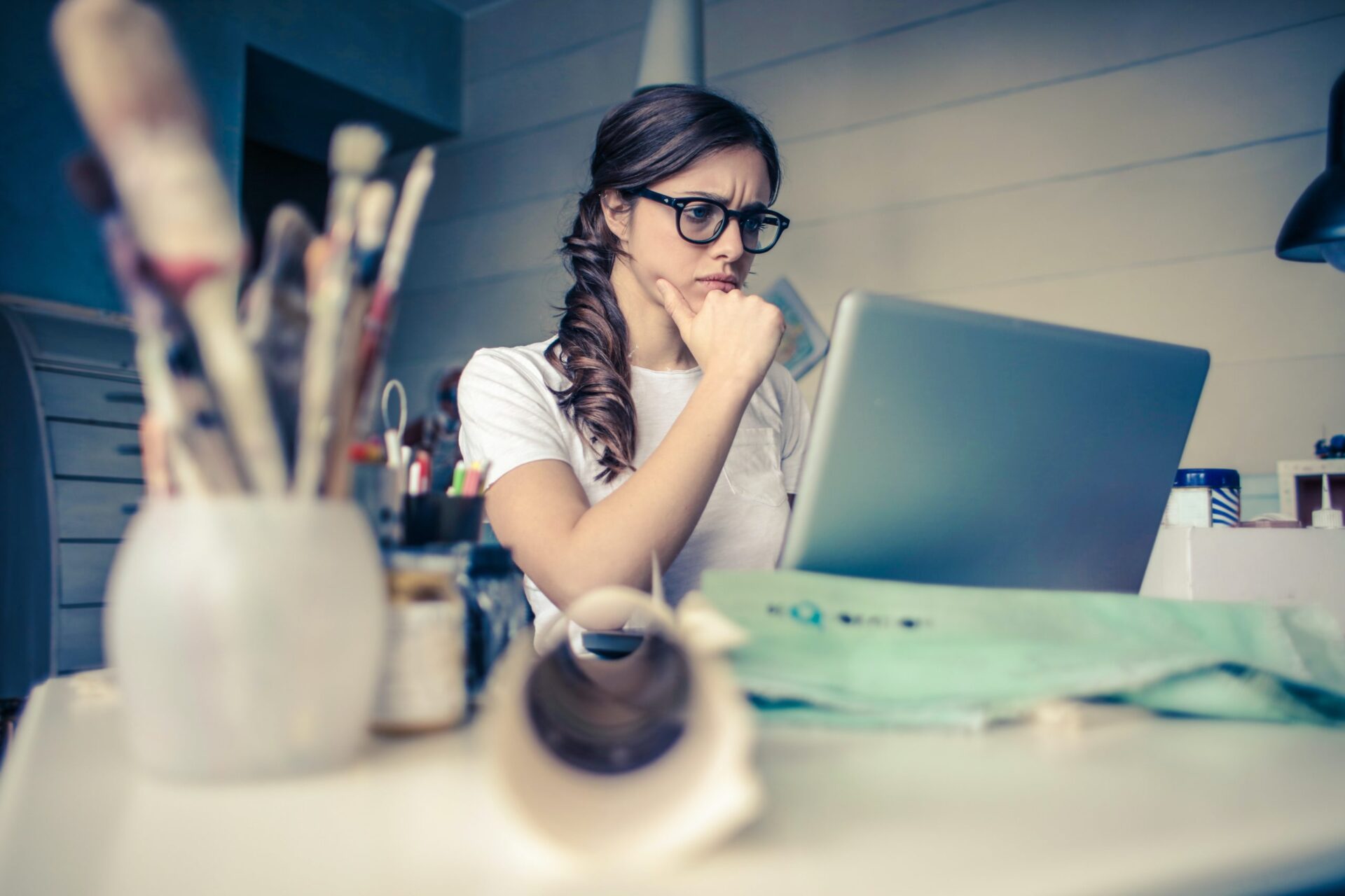 Woman working at a laptop at a cluttered desk with art supplies around