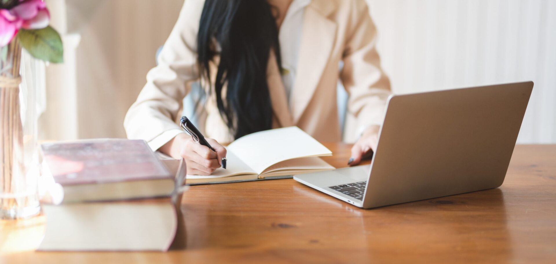Woman working at a laptop and writing in a notebook