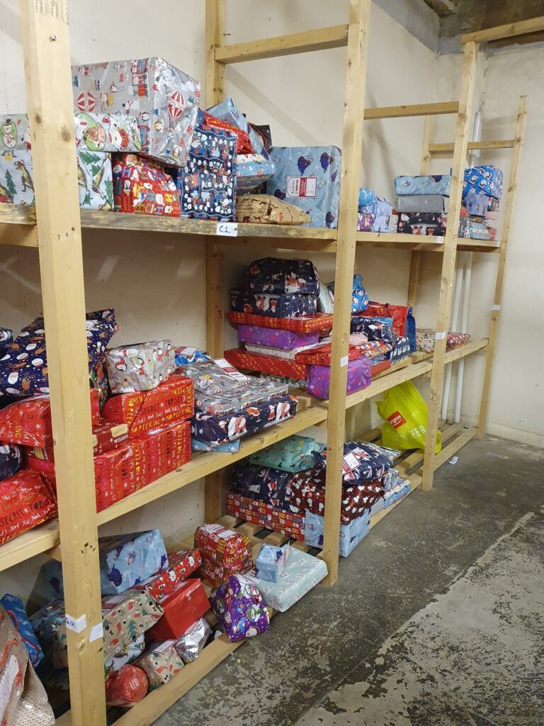 Unopened Christmas presents on a shelving unit in a charity