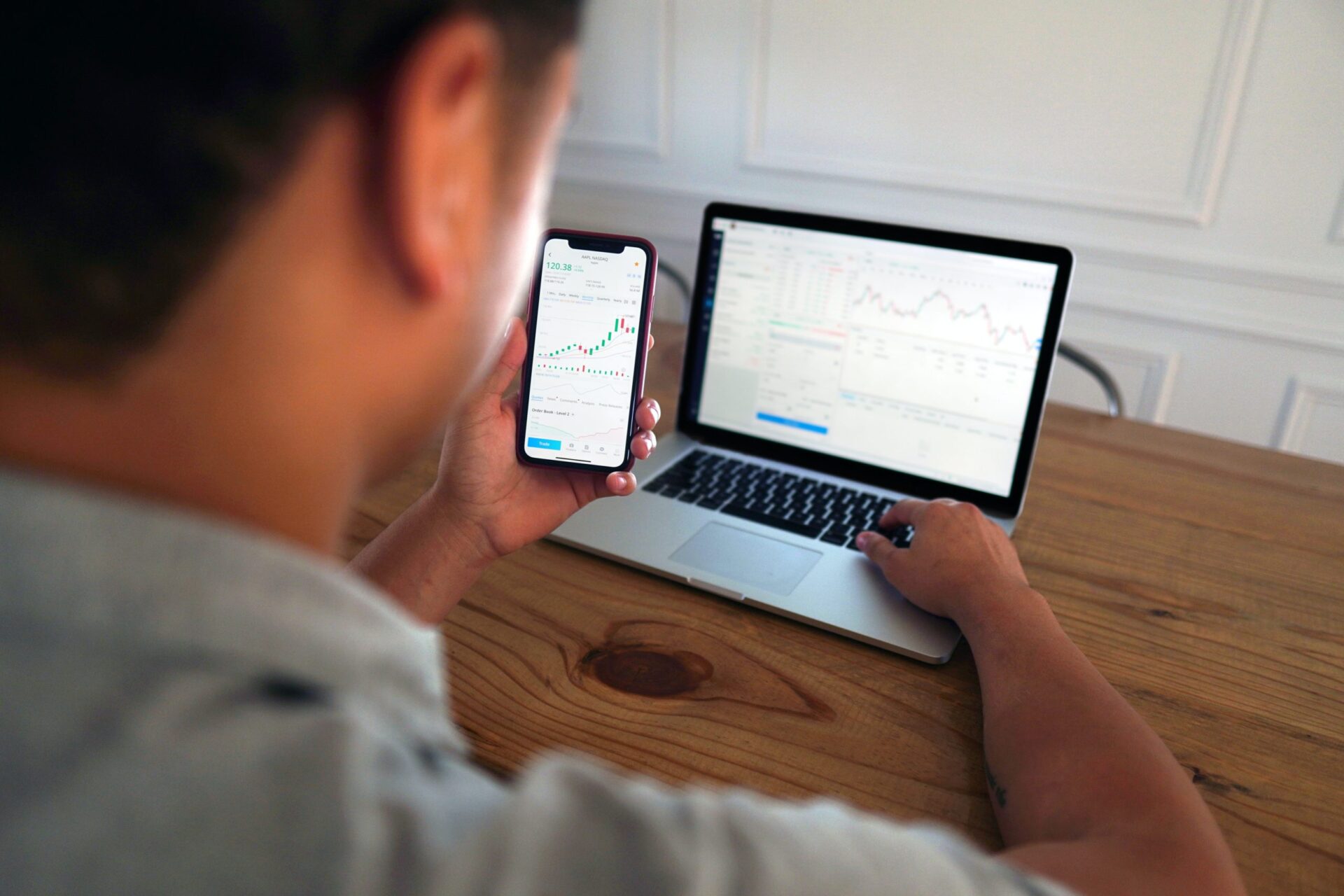 Man working at a laptop and looking at graphs on his mobile phone