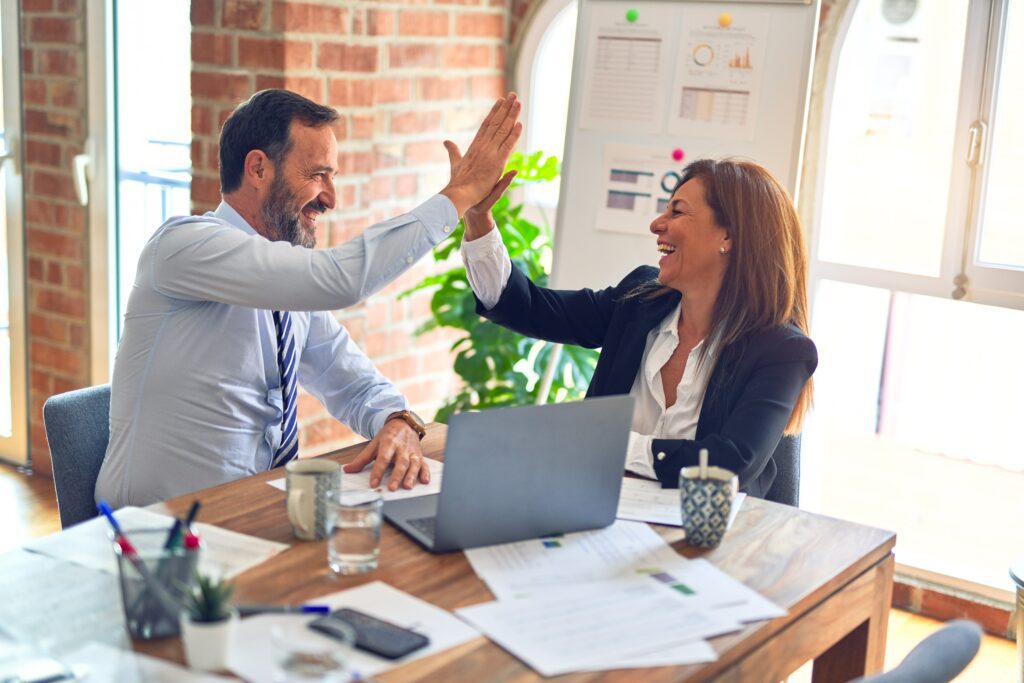 Two business people sat at a laptop hi-fiving over their work
