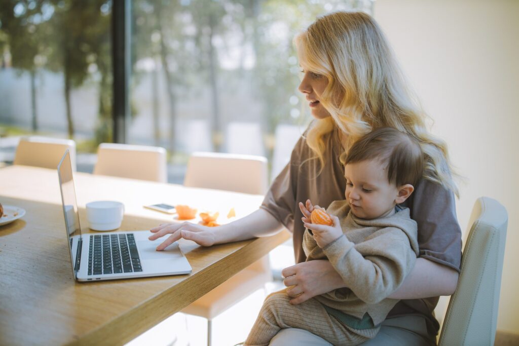 A mother doing flexible working holding her child as she works at a laptop