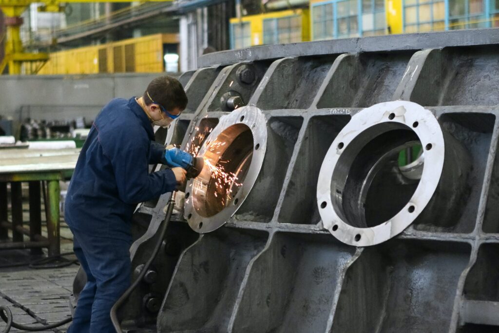 A man in a manufacturing factory using an angle grinder on a large metal object