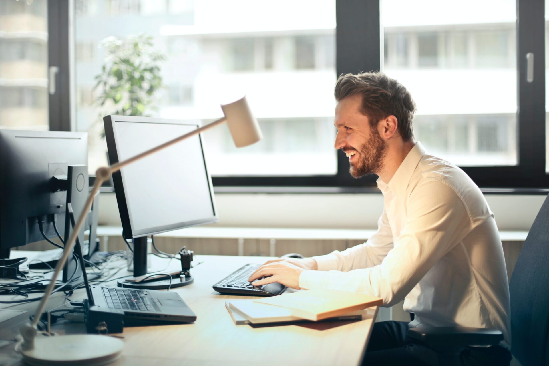 A man working at a laptop at a work desk and smiling at something on the screen