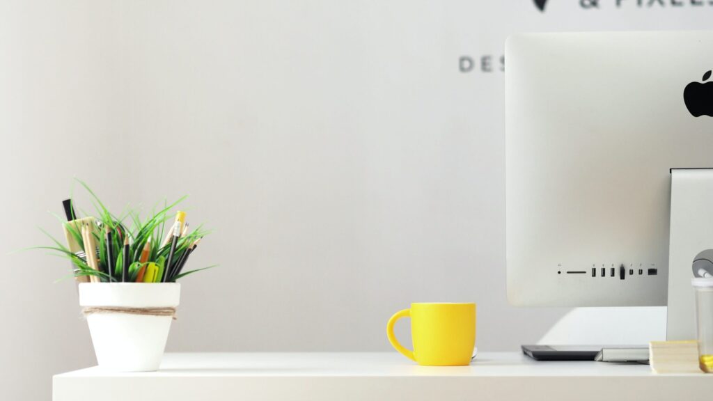 Bright image of a tidy desk with a yellow mug and plant pot with pens in
