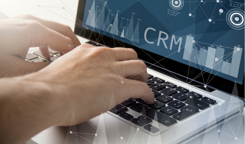 Closeup of hands typing on a laptop that displays charts and graphs and the letters CRM