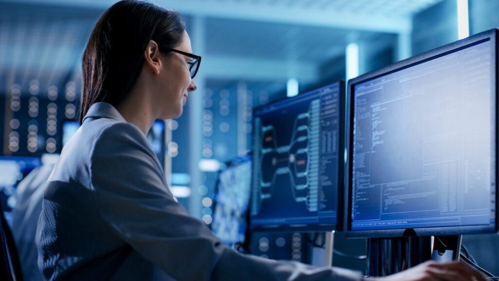 Female IT engineer working at a computer with multiple screens working on coding