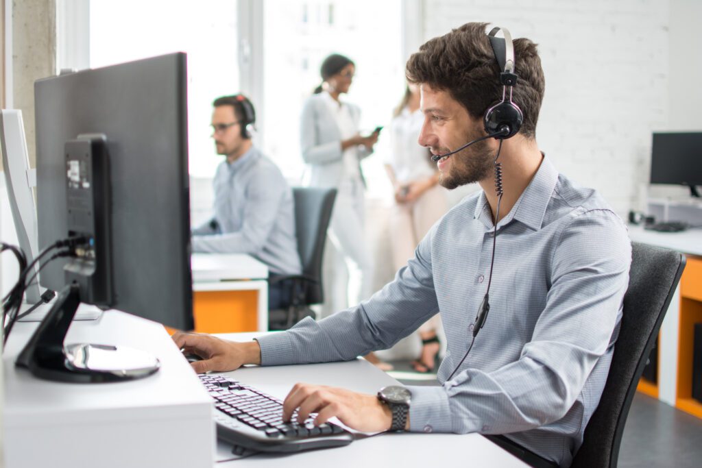 Smiling tech support operator sat at a computer and speaking with a client using a headset