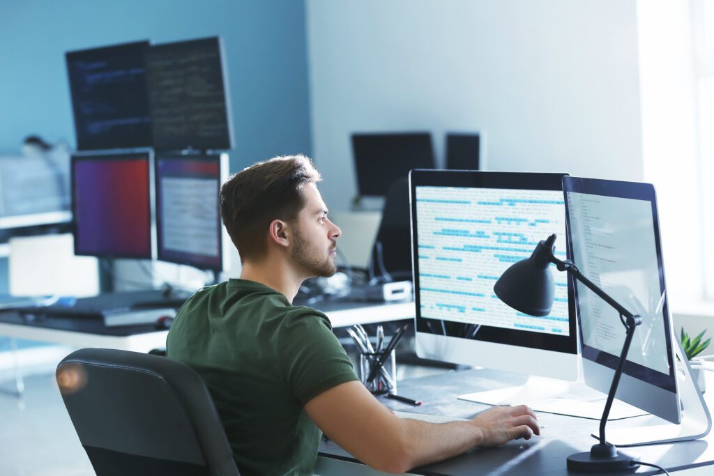 Male programmer working at a computer with multiple screens in an office