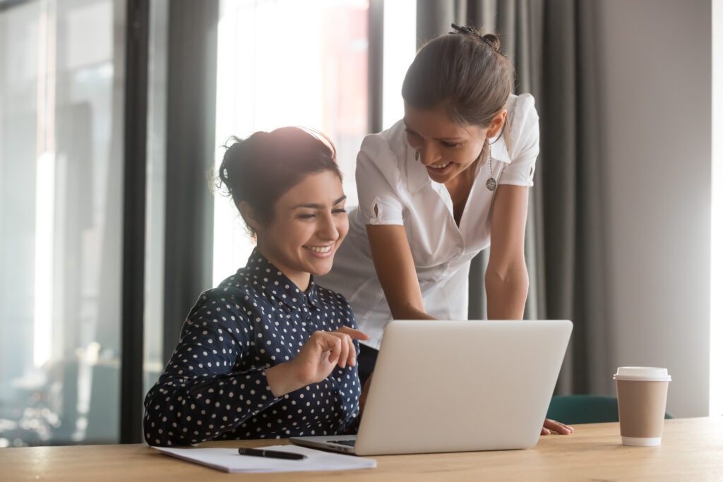 Smiling mentor helping someone at a laptop