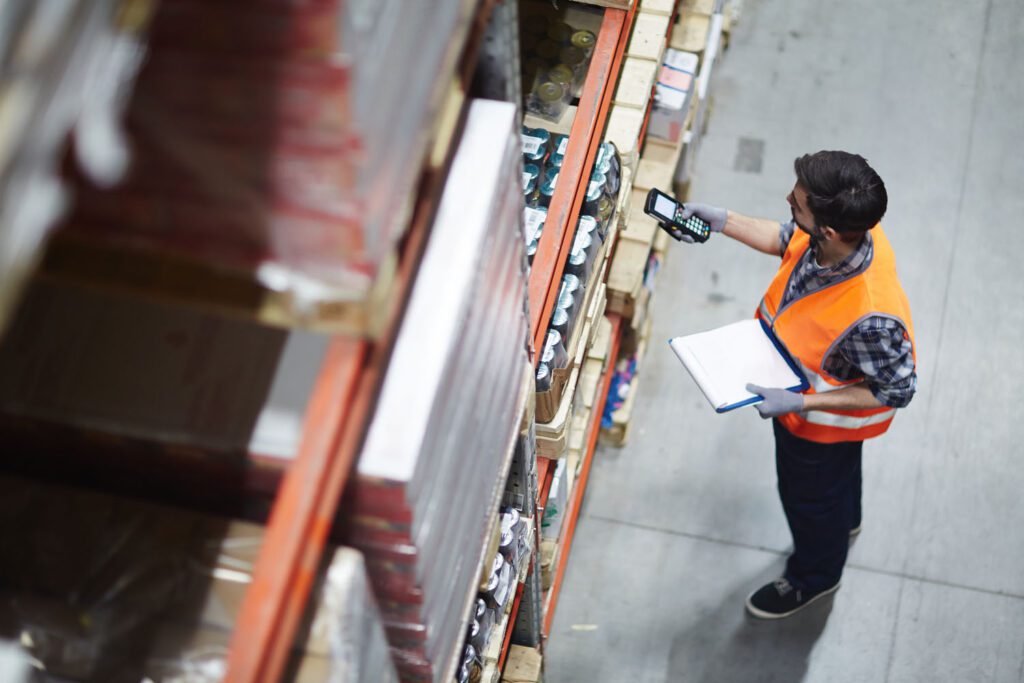 Topdown view of a warehouse worker in a hi vis vest checking an order with a scanner and clipboard