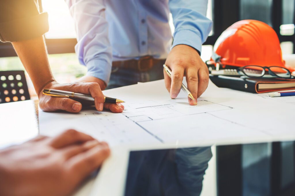 Closeup of architectural drawings on a desk as several people point at and make notes