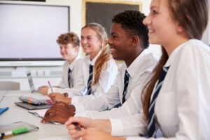 Group of school students in uniform at a desk working and speaking to the teacher