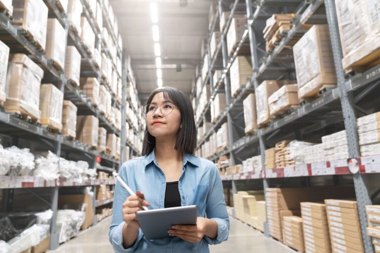 Young businesswoman walking through a warehouse and checking stock using a tablet