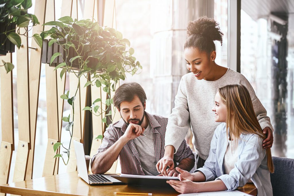 Happy multiracial millennial colleagues discussing company financial statistics at briefing in office, employees brainstorming analyzing growing sales, developing success strategies, reading reports