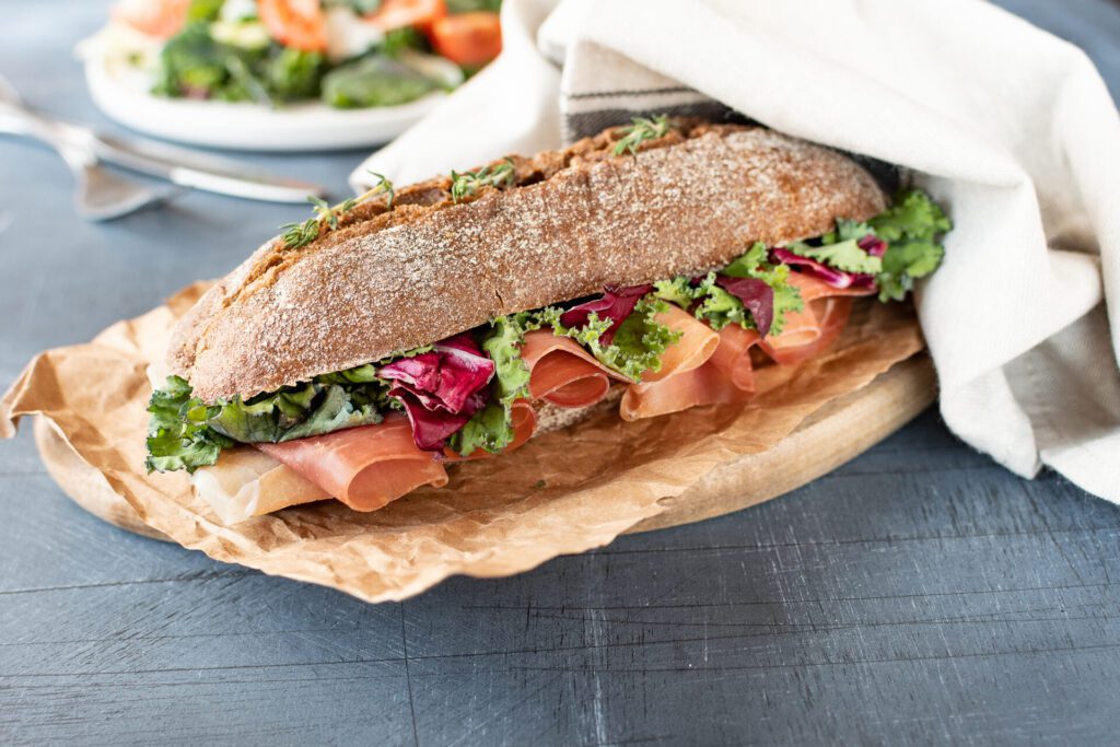 A sandwich made with a baguette with lettuce and ham poking out of the cut side