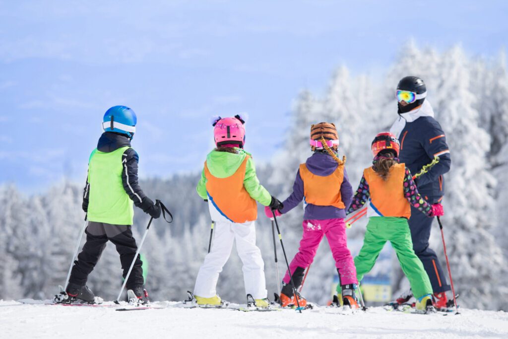 Group of children on a skiing lesson wearing bright clothing against a grey blue sky