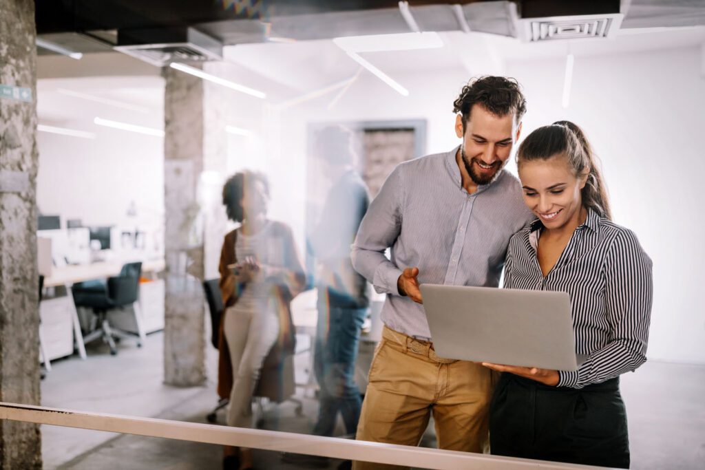 Two young business people in a casual open plan office looking at a laptop and smiling
