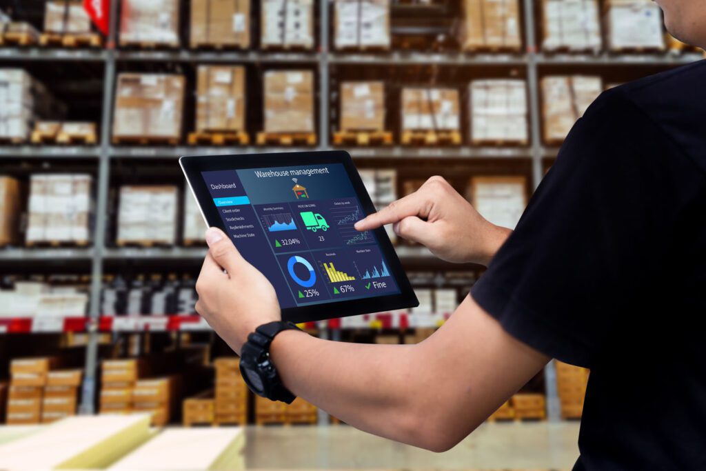 Warehouse management system. Worker holding a tablet against blurred warehouse as background