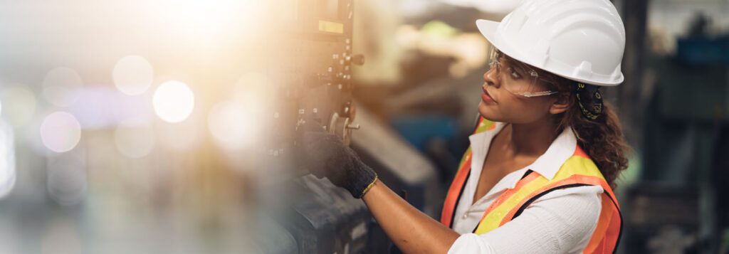 Woman engineer wearing hi vis and safety equipment working at a machine in a factory