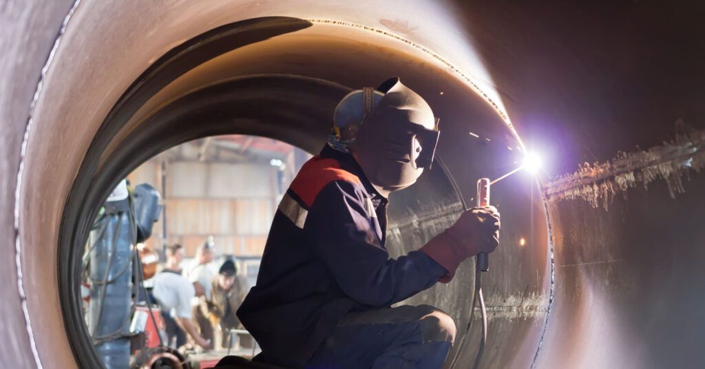 A worker welding inside a large metal pipe