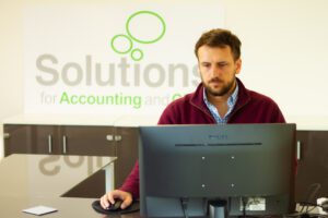 Solutions employee working at a computer with a large sign saying Solutions for Accounting in the background