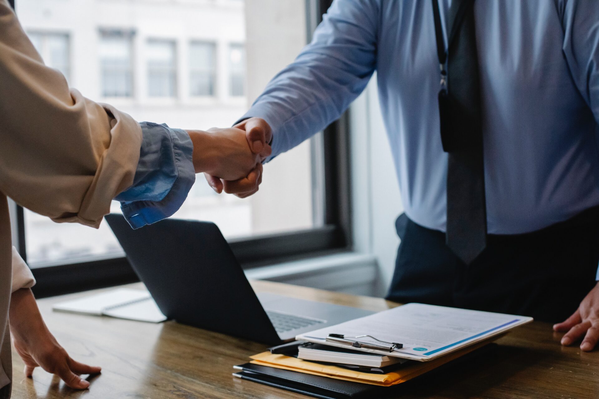 Two people shaking hands over a desk with a laptop