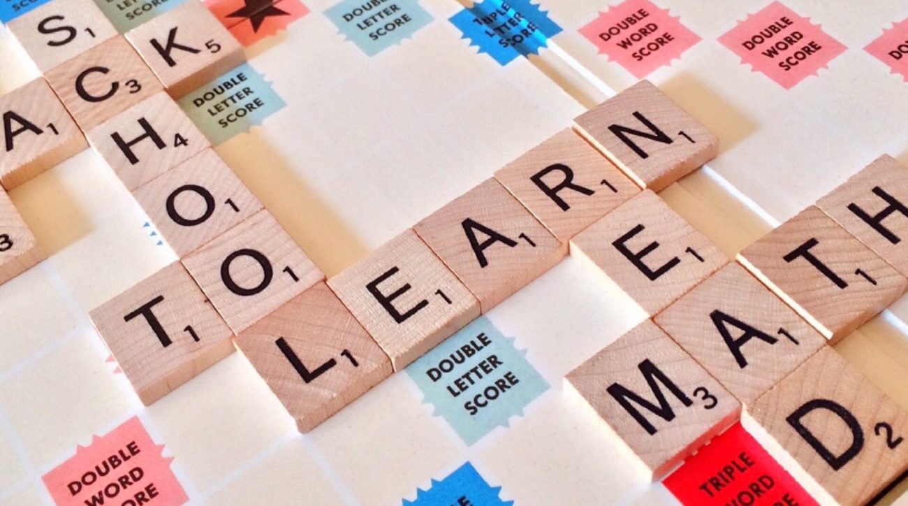 Scrabble tiles on a scrabble board layout out words that read schools, to, lead, read, and maths