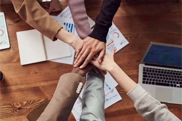 six peoples hands one on top of the other as in a team huddle