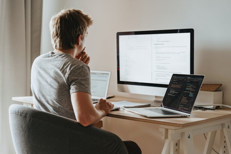 Young man working at a desk with three computer screens open