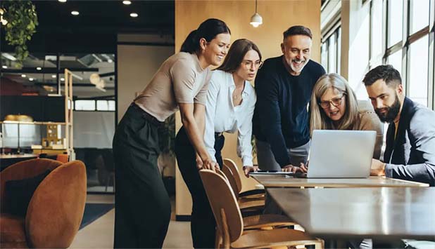 Five people looking at a laptop in an open office