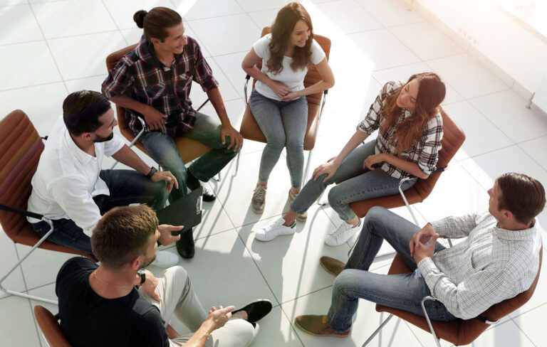 Group of young adults sitting on chairs in a circle having a discussion