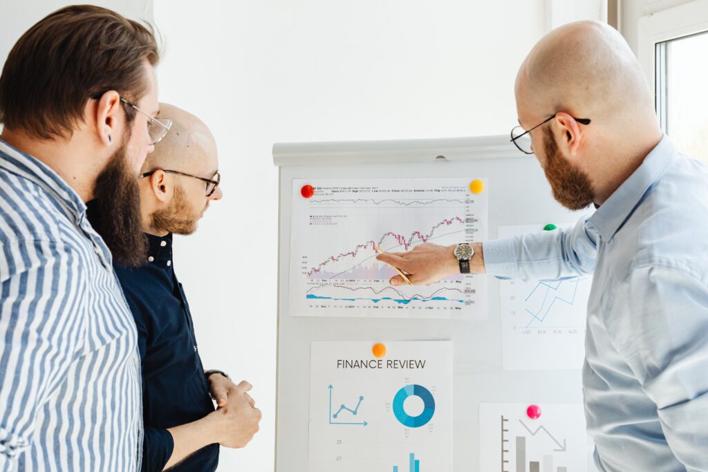 Three business men pointing at financial charts titled Finance Review