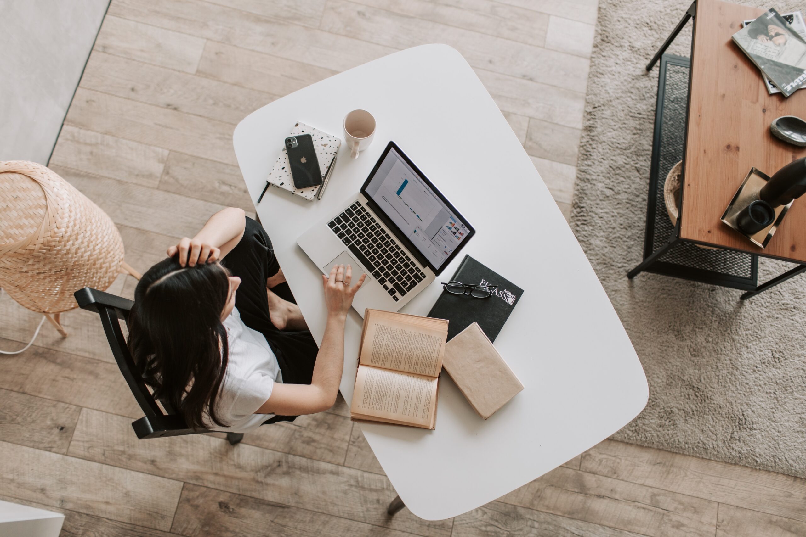 Overhead photo of a woman working at laptop on a desk with an open book next to her