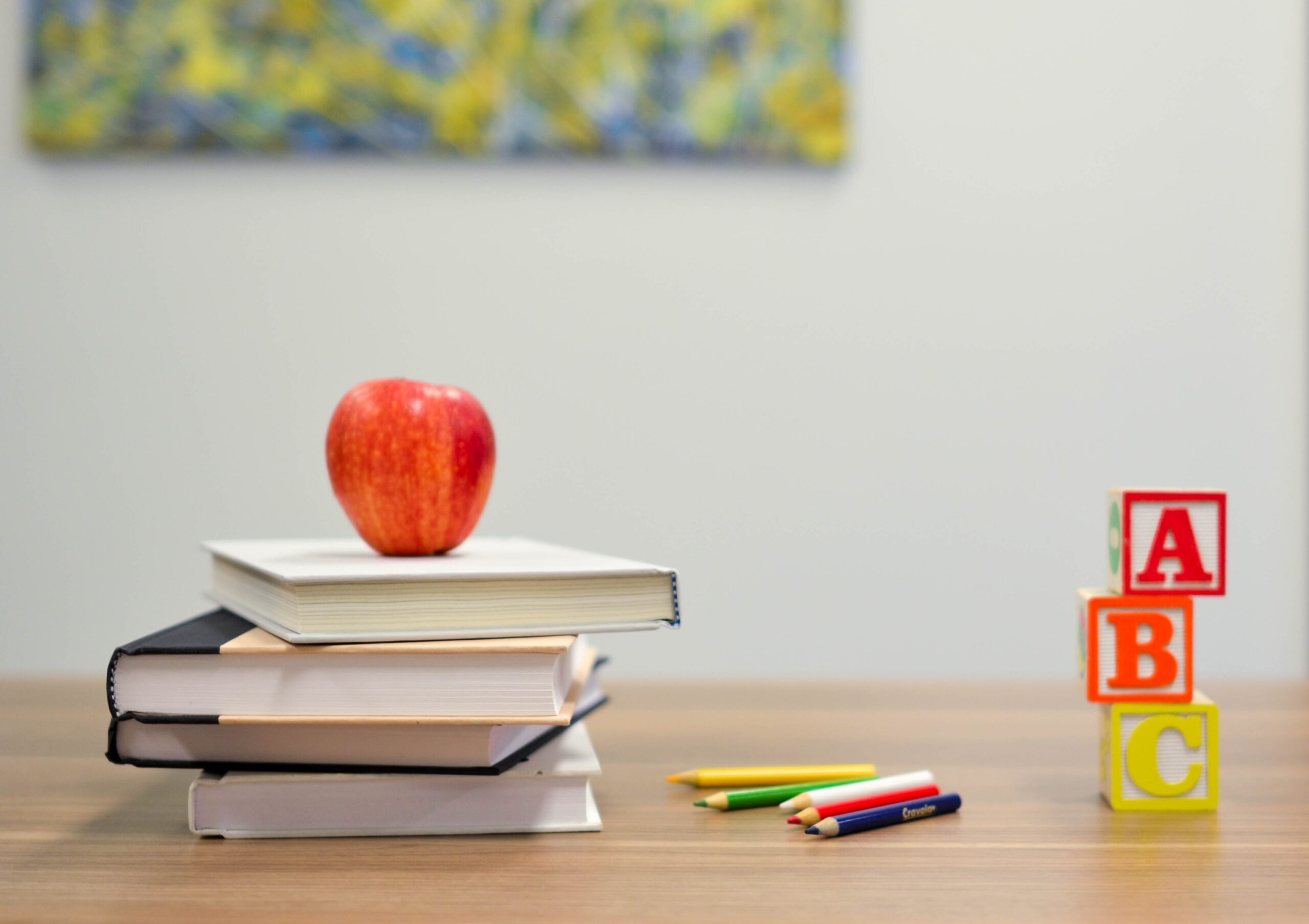 Apple resting on a stack of books next to coloured pencils and lettered blocks