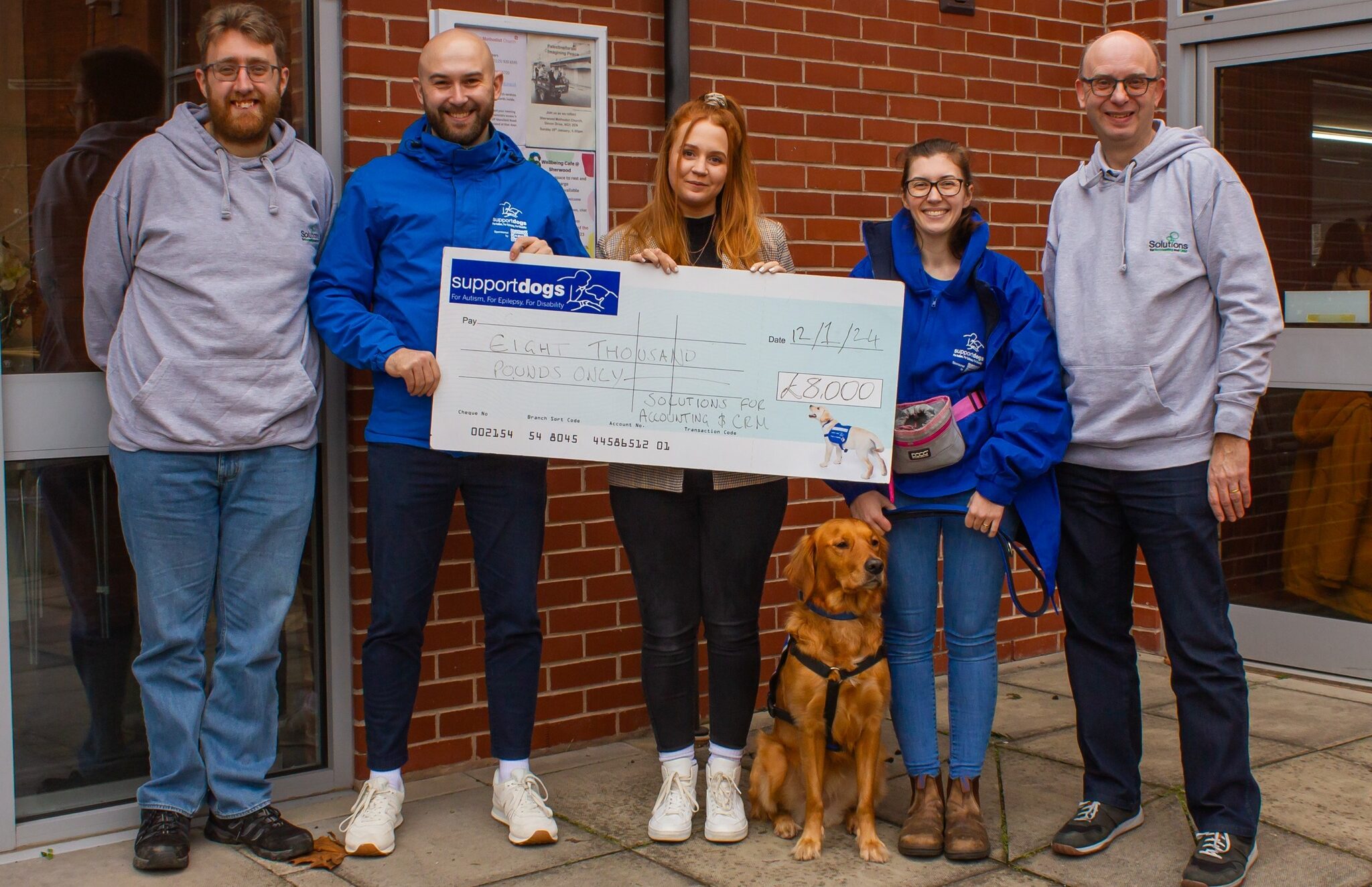 Several employees from Solutions for Accounting holding a large cheque of money raised for the charity Support Dogs