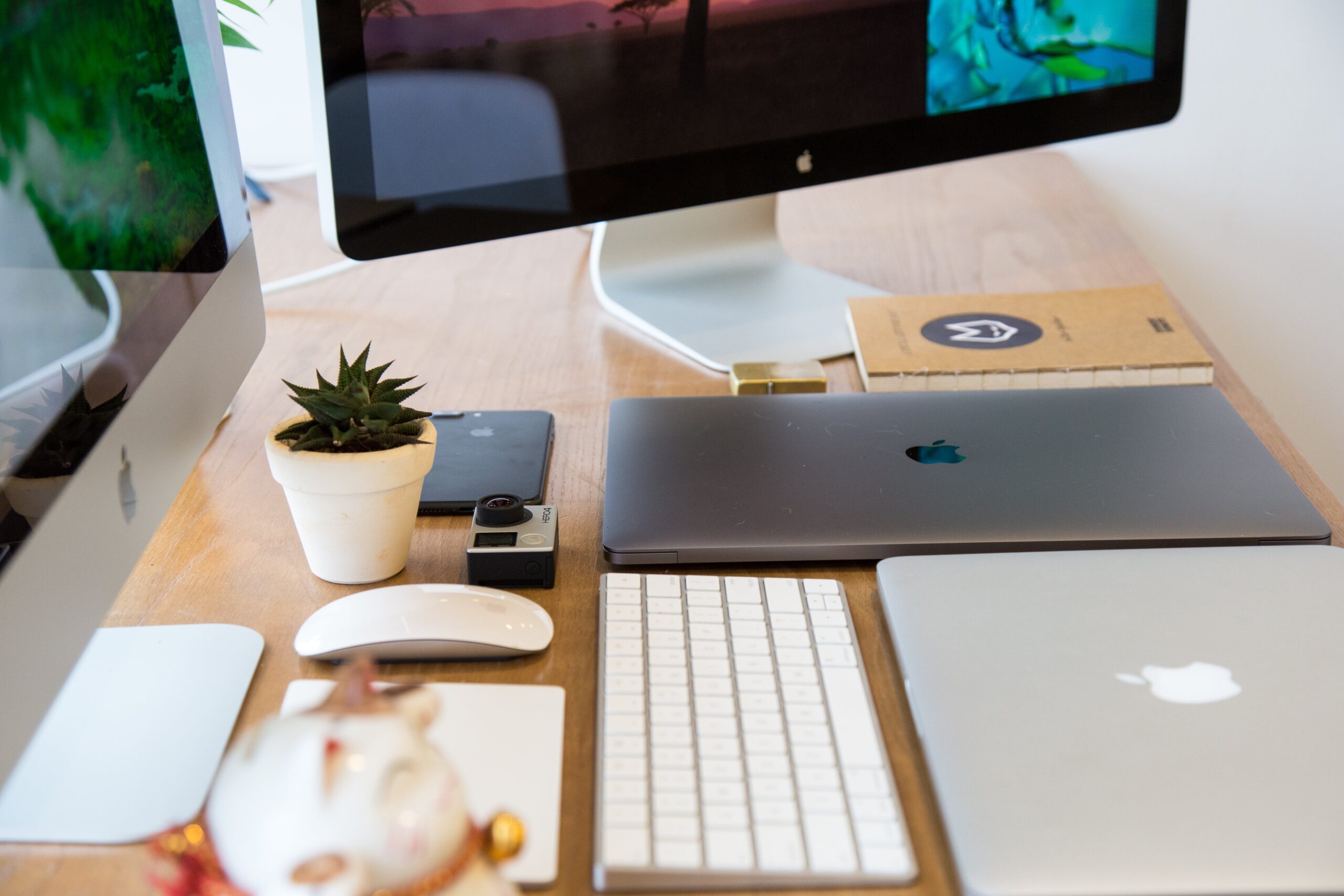 Closeup of a desk with two computer monitors, laptops, an action camera and a notebook