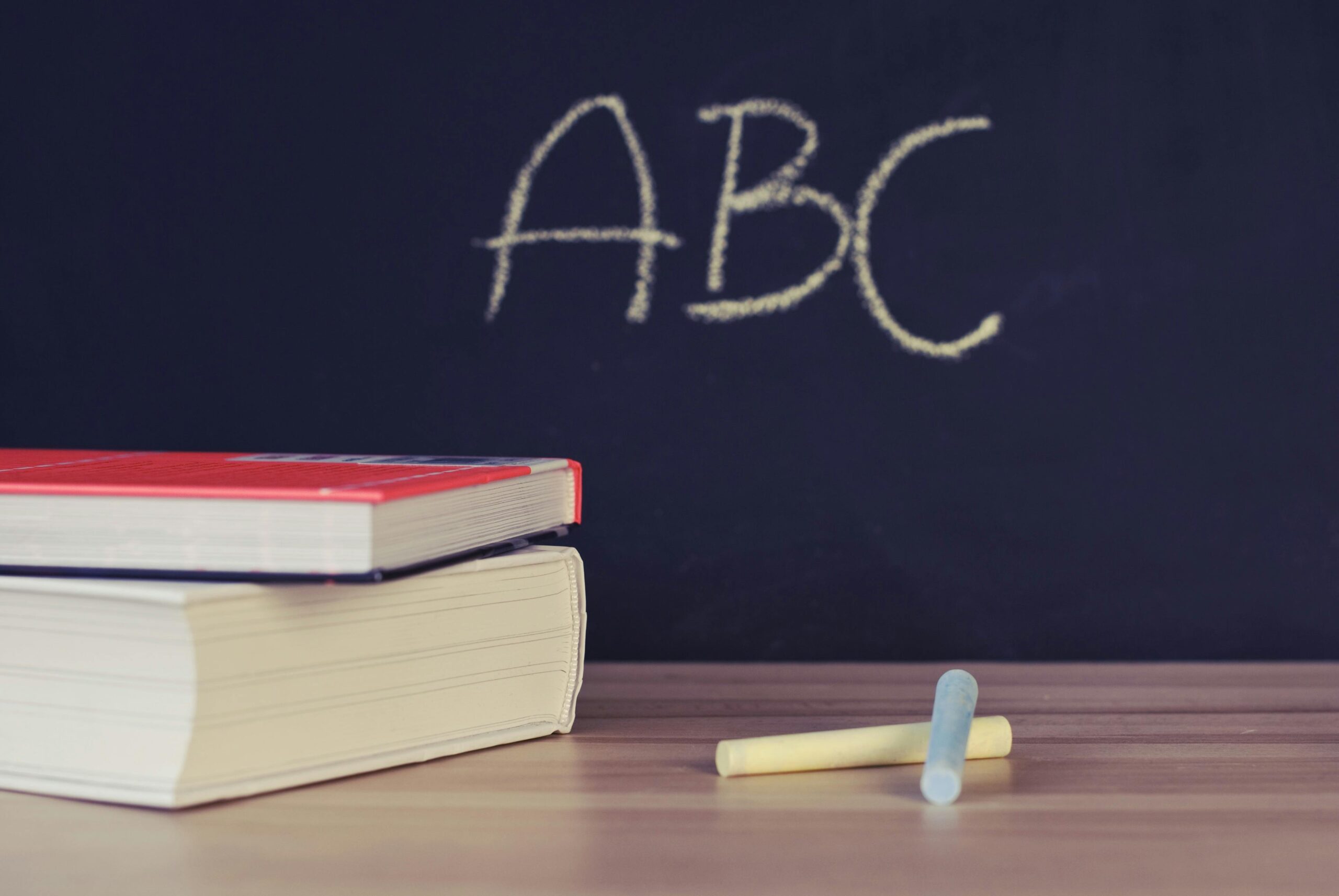 ABC written on a chalkboard with books and chalk laying in front of it