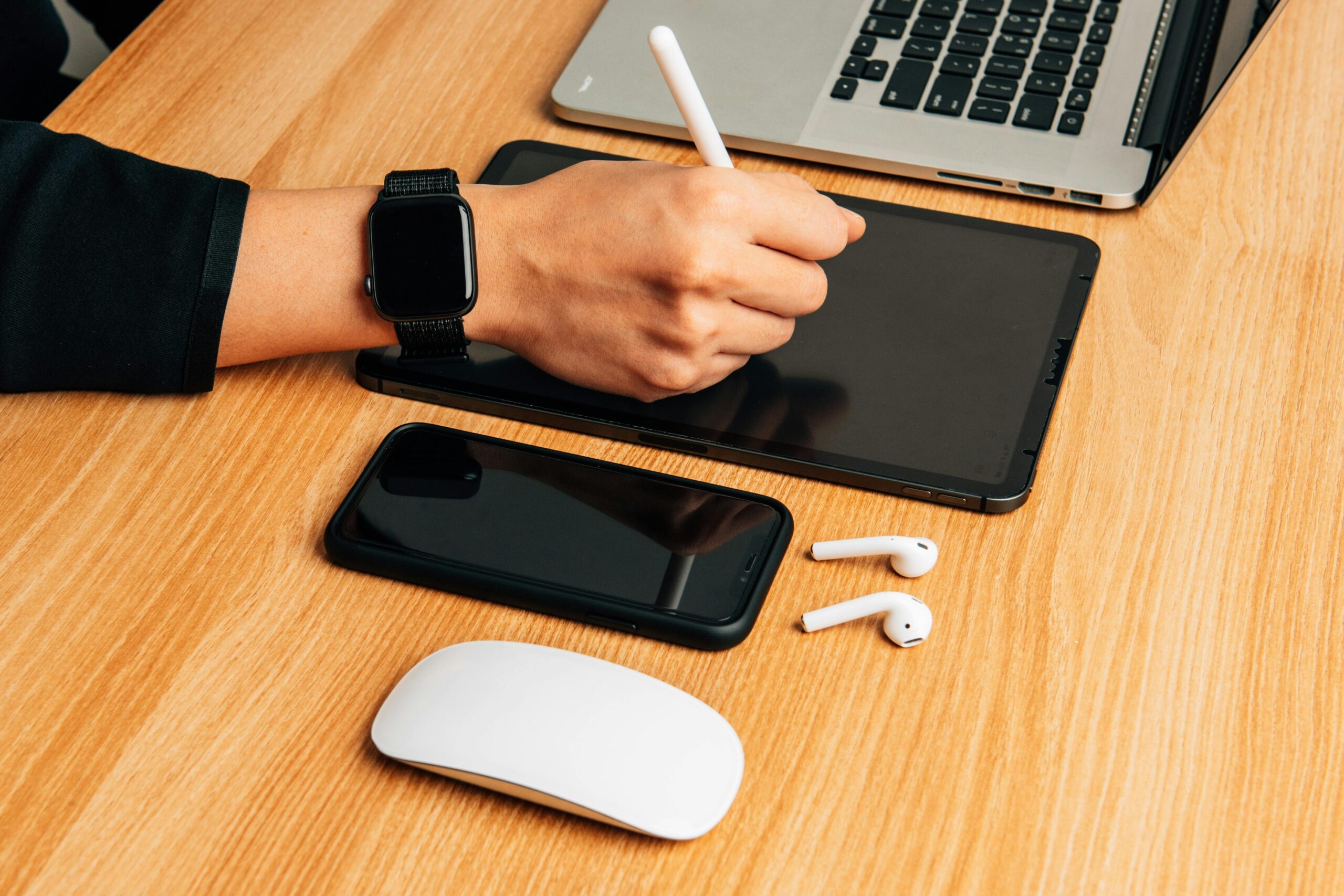 Closeup of someone working at a desk with several electronic devices like a laptop, tablet and smart phone