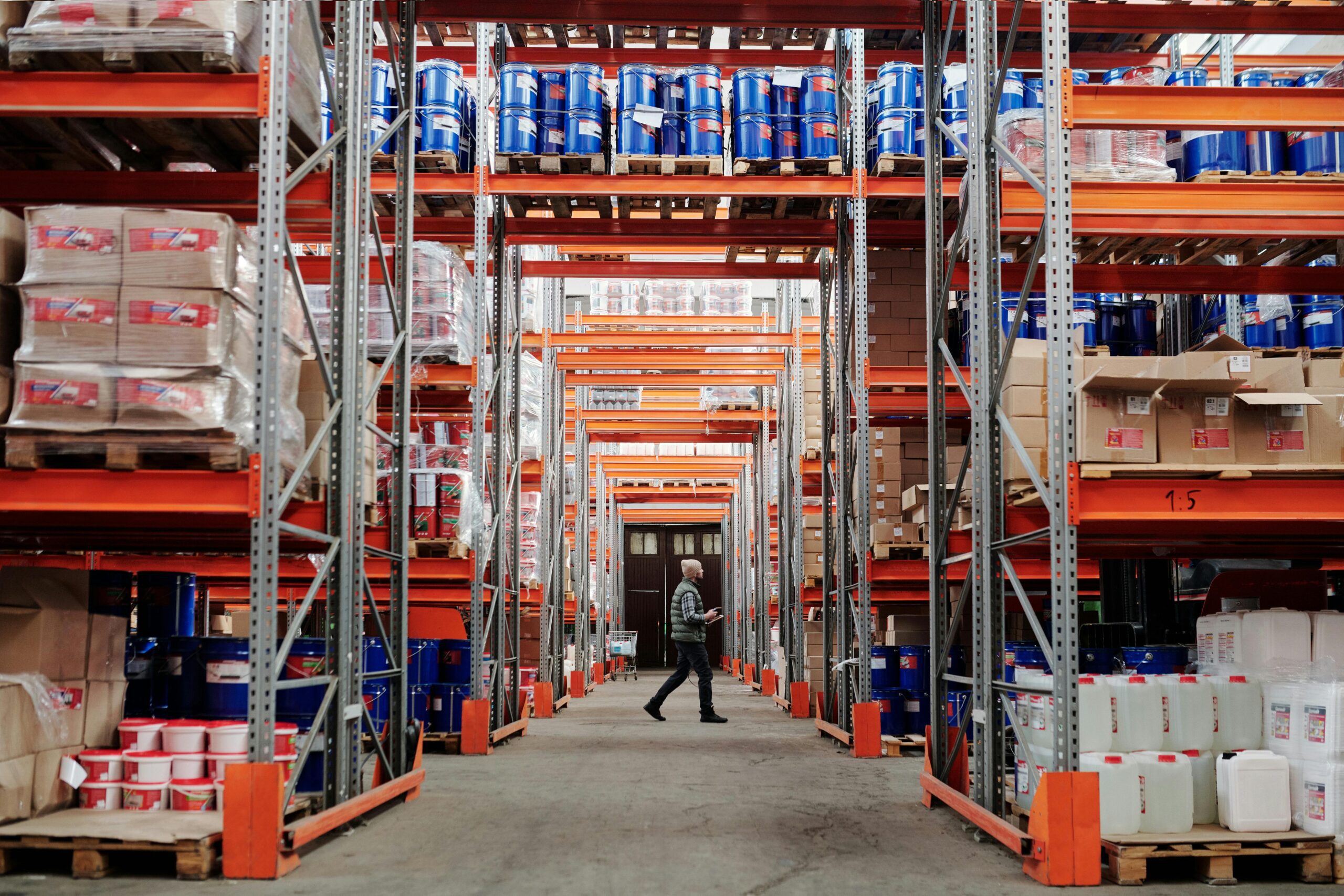 Wide photo of a warehouse filled with stock on shelving as a worker walks through them