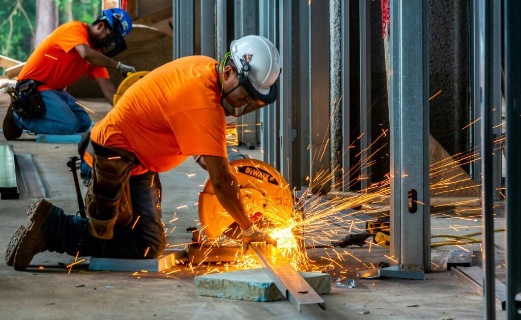 Man working in manufacturing uses a power tools to cut through a bar of metal