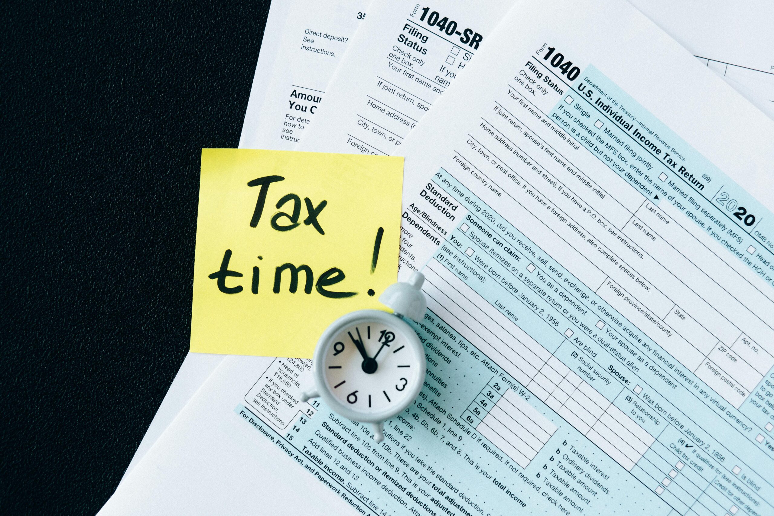 Bundle of tax documents with a clock on top and a sticky note reading Tax Time!