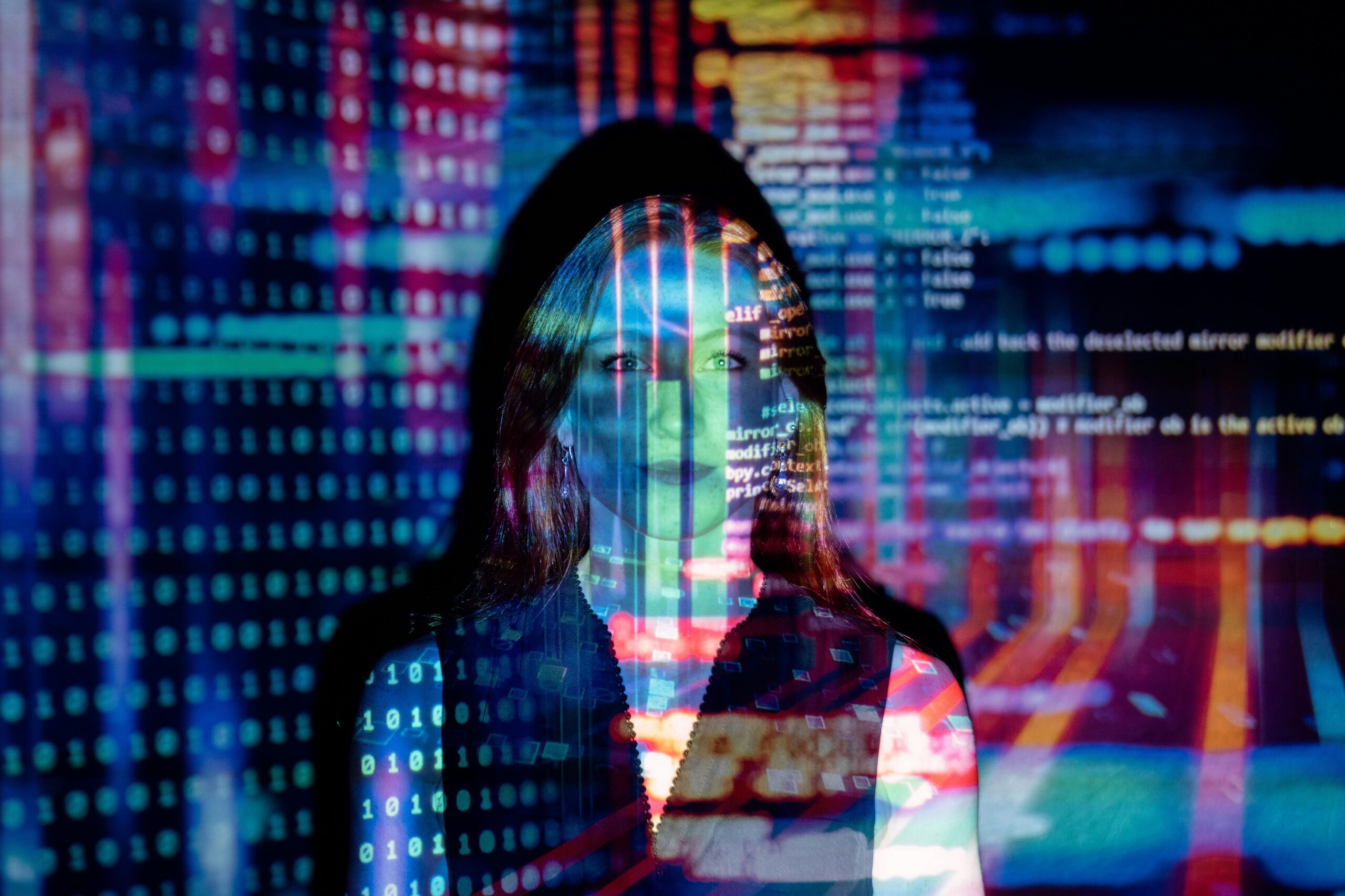 Woman against a wall with lots of coding being projected onto her and the wall behind her, symbolising the combination of human and machine intelligence