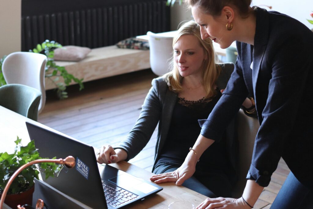 Two women talking about something on a laptop on a desk in a casual office setting