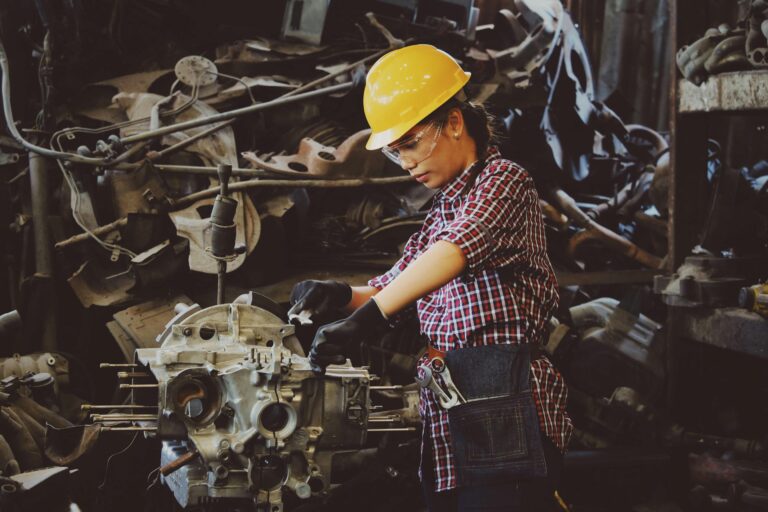 Woman working in a factory using machinery and surrounded by heavy metal objects